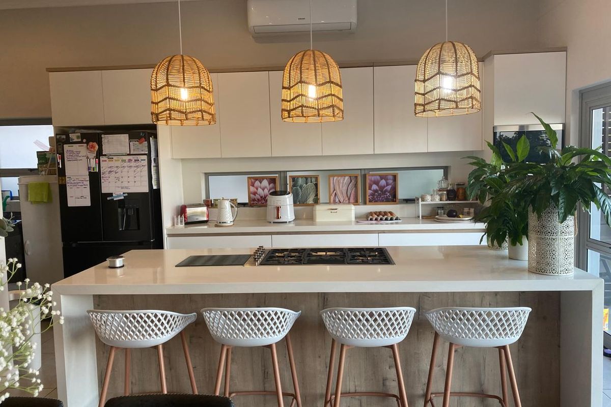Modern kitchen featuring a large island with a built-in gas cooktop, sleek white cabinetry, stone countertops, and contemporary pendant lighting.