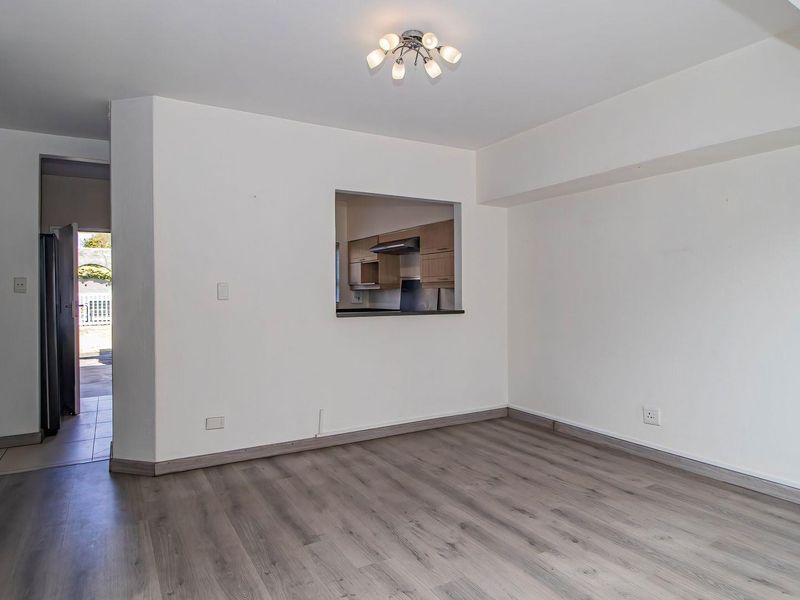 An empty living room featuring modern laminate flooring and a convenient pass-through window connecting to the kitchen area.