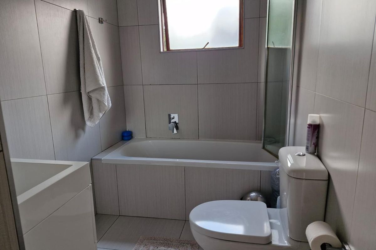 A functional bathroom featuring a built-in bathtub with shower mixer, a modern toilet, and neutral wall tiling throughout.