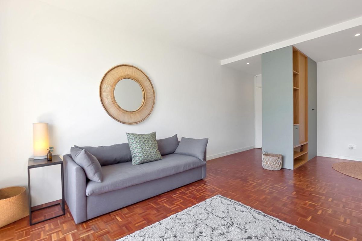 A bright living room featuring warm parquet flooring, a modern built-in shelving unit, and recessed ceiling lighting.