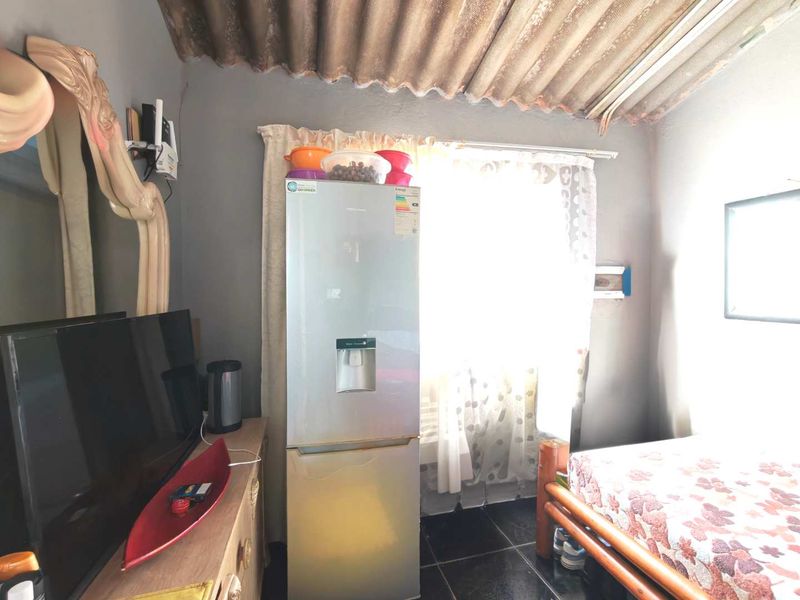 A compact bedroom featuring tiled flooring and an exposed corrugated roof structure, requiring cosmetic updates to improve the overall finish and aesthetic.