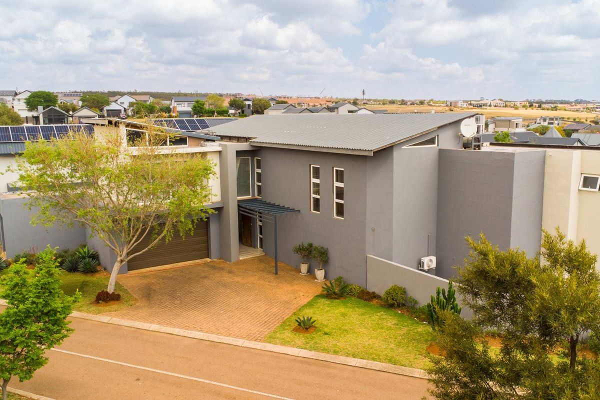 Aerial view of a modern two-story residential property featuring a paved driveway, garage, and solar panel installation on the roof.