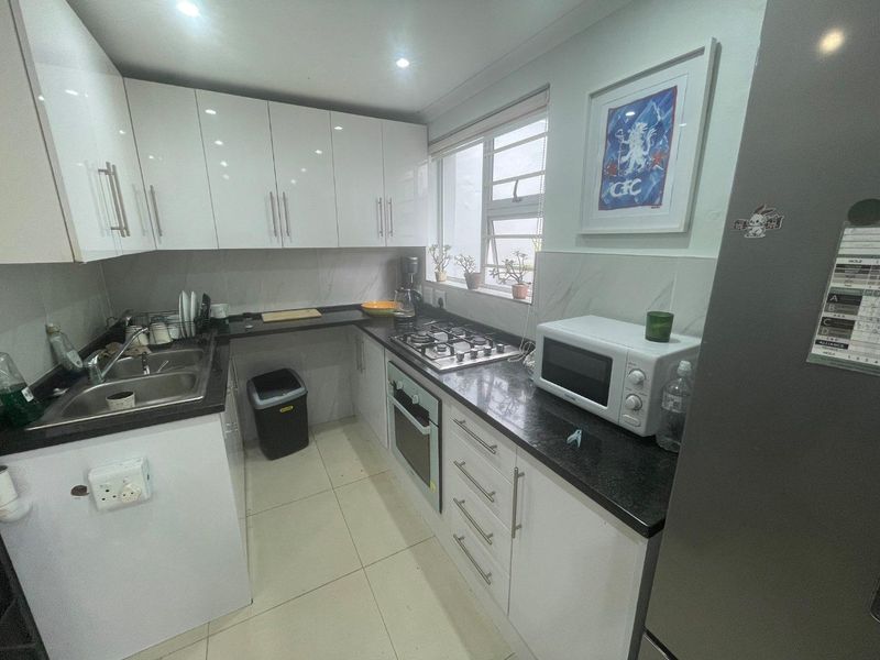 A modern kitchen featuring white high-gloss cabinetry, dark granite countertops, a gas hob, built-in oven, and tiled flooring.