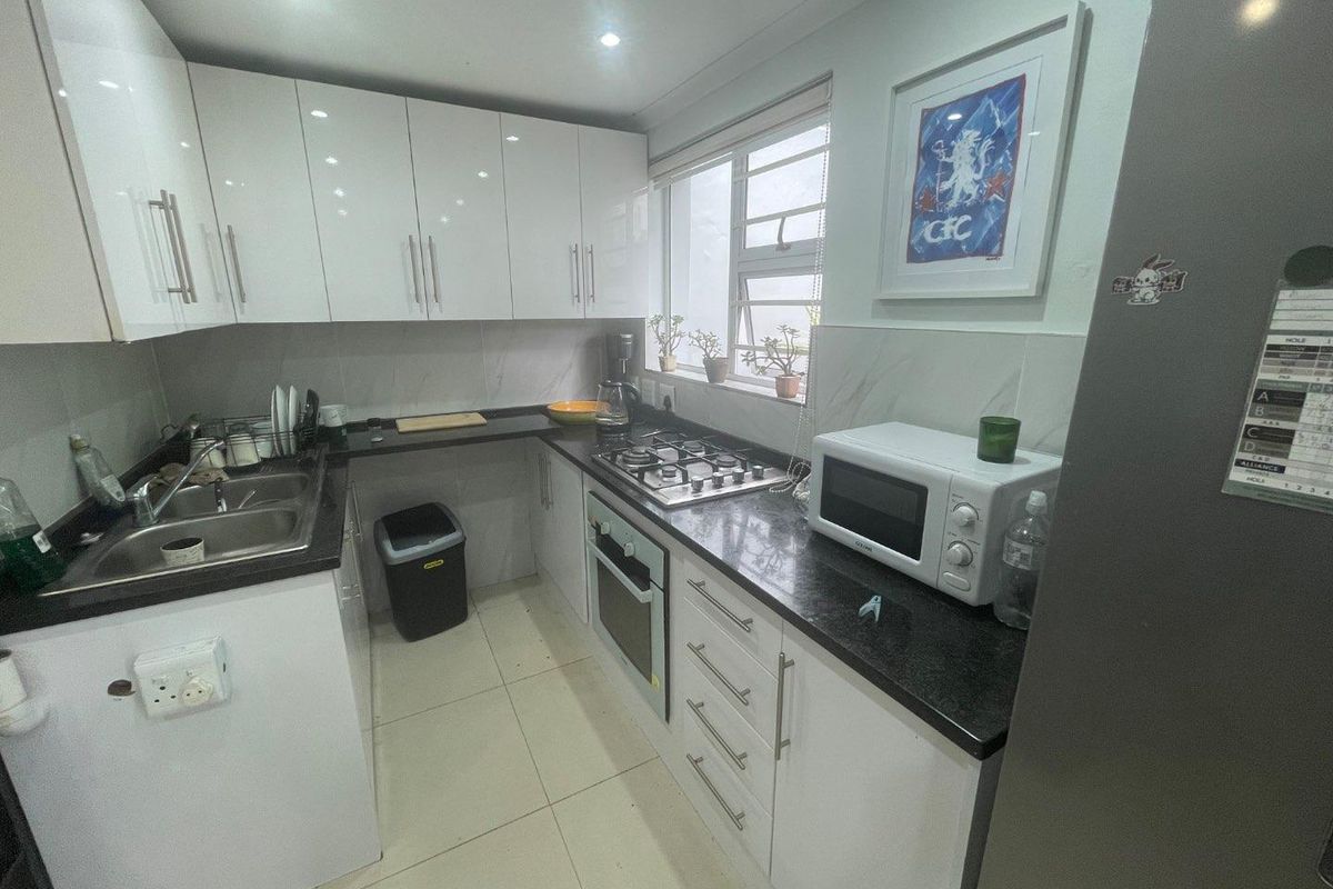 A modern kitchen featuring white high-gloss cabinetry, dark granite countertops, a gas hob, built-in oven, and tiled flooring.