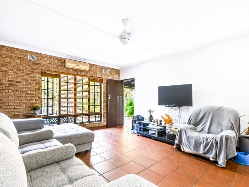 A living room featuring exposed brick walls, ceramic tile flooring, a ceiling fan, and a split-system air conditioner, with direct access to an outdoor area.