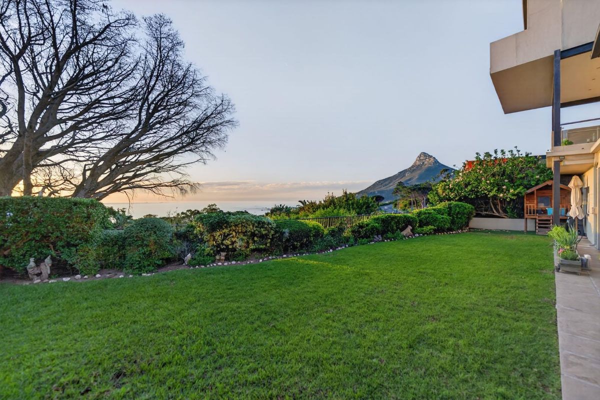 A well-maintained rear garden featuring a lush lawn, landscaped borders, and a paved patio area with scenic mountain and ocean views.