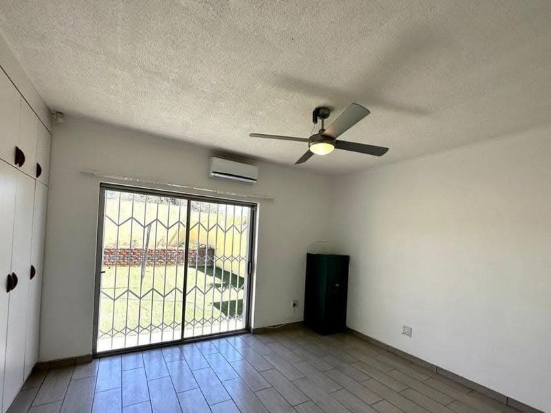 A bright bedroom featuring built-in cupboards, a ceiling fan, air conditioning, and a sliding door providing direct access to the rear garden.