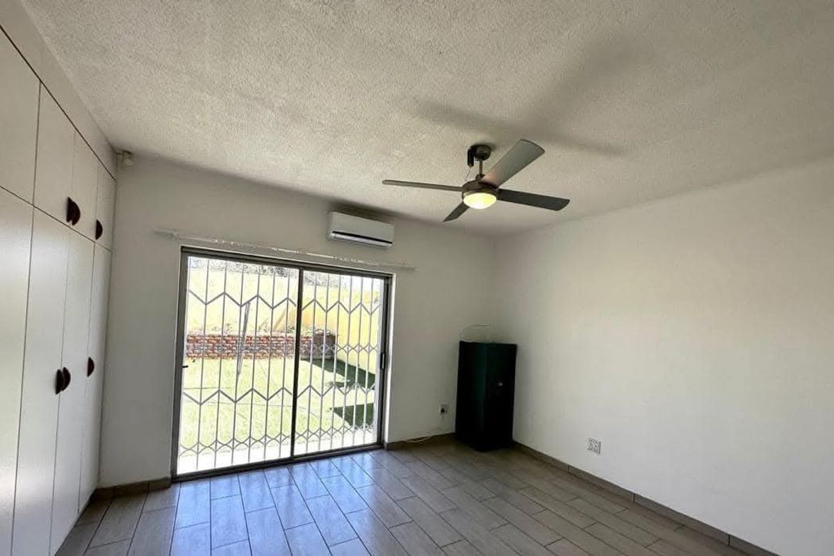 A bright bedroom featuring built-in cupboards, a ceiling fan, air conditioning, and a sliding door providing direct access to the rear garden.