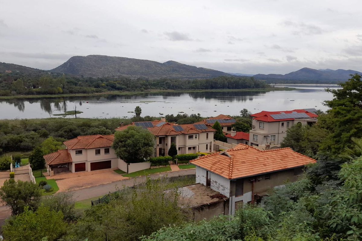Elevated aerial view overlooking a residential estate with tiled roofs, solar panels, and a scenic lake and mountain backdrop.