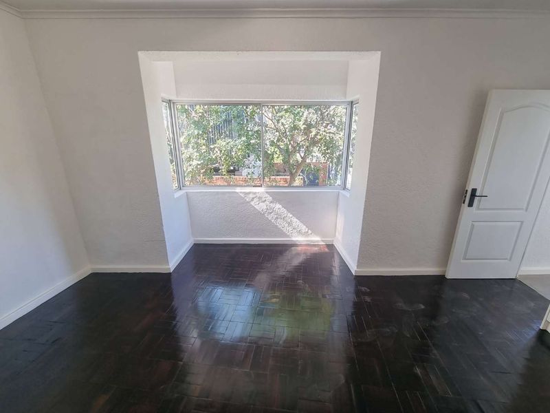 An empty bedroom featuring dark parquet flooring, a large bay window providing natural light, and a classic panel door.
