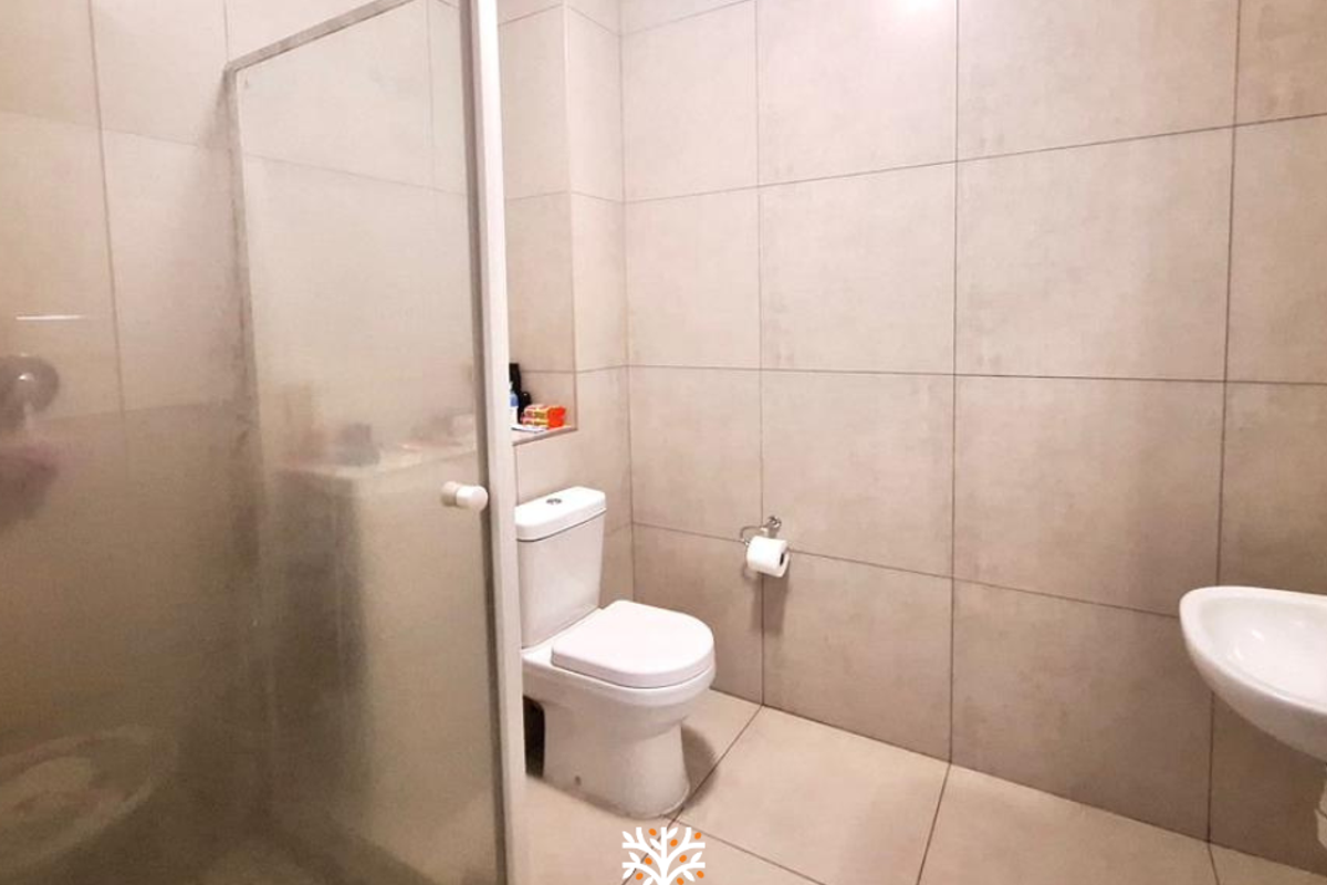 A modern bathroom featuring large-format neutral wall and floor tiles, a glass-enclosed shower, a white toilet, and a wall-mounted basin.