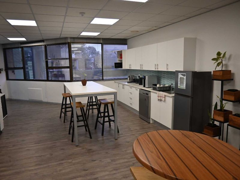 A functional office kitchenette featuring modern white cabinetry, a tiled backsplash, integrated dishwasher, and durable laminate flooring with ample natural light.