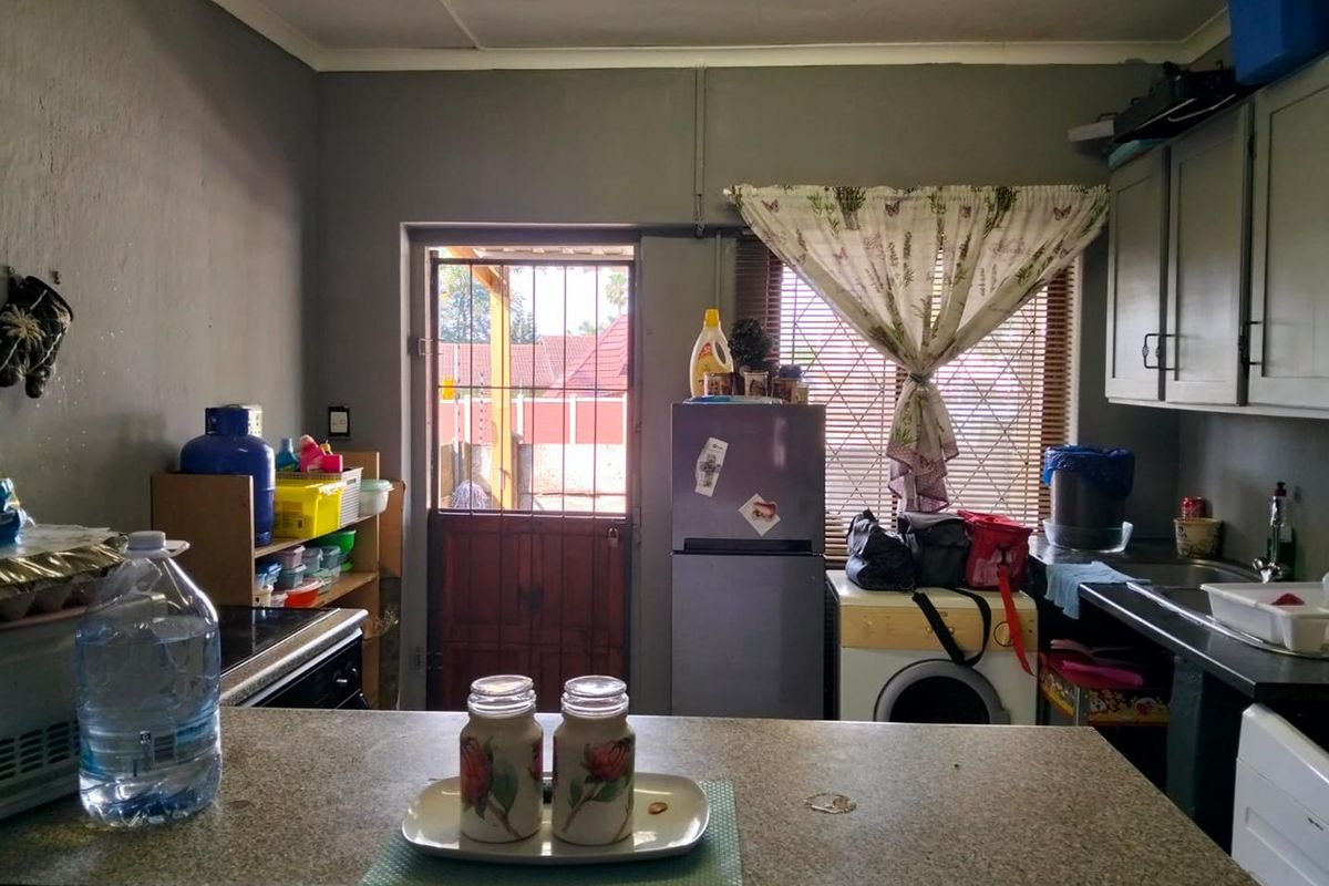 A functional kitchen featuring laminate countertops, built-in cabinetry, and a rear access door with security gate, offering potential for modernization.