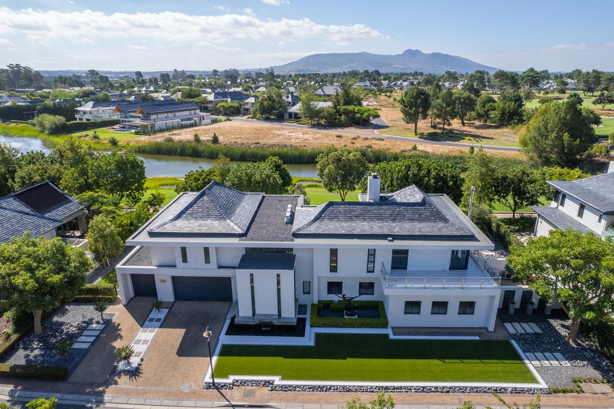 Aerial view of a modern luxury residence featuring a slate roof, double garage, balcony, and manicured garden, set within a scenic estate landscape.