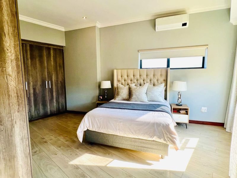 A well-maintained bedroom featuring light laminate flooring, built-in wooden cupboards, and a wall-mounted air conditioning unit.