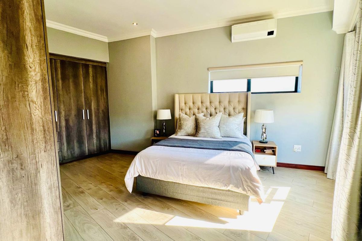 A well-maintained bedroom featuring light laminate flooring, built-in wooden cupboards, and a wall-mounted air conditioning unit.