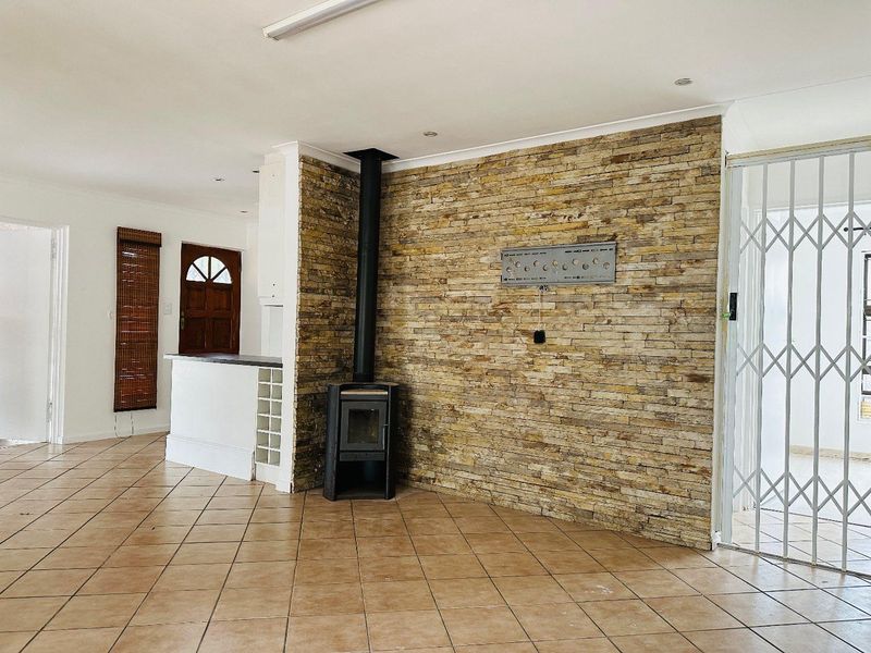 Spacious living area featuring a prominent stone accent wall, a freestanding fireplace, and ceramic tiled flooring with a breakfast bar transition.