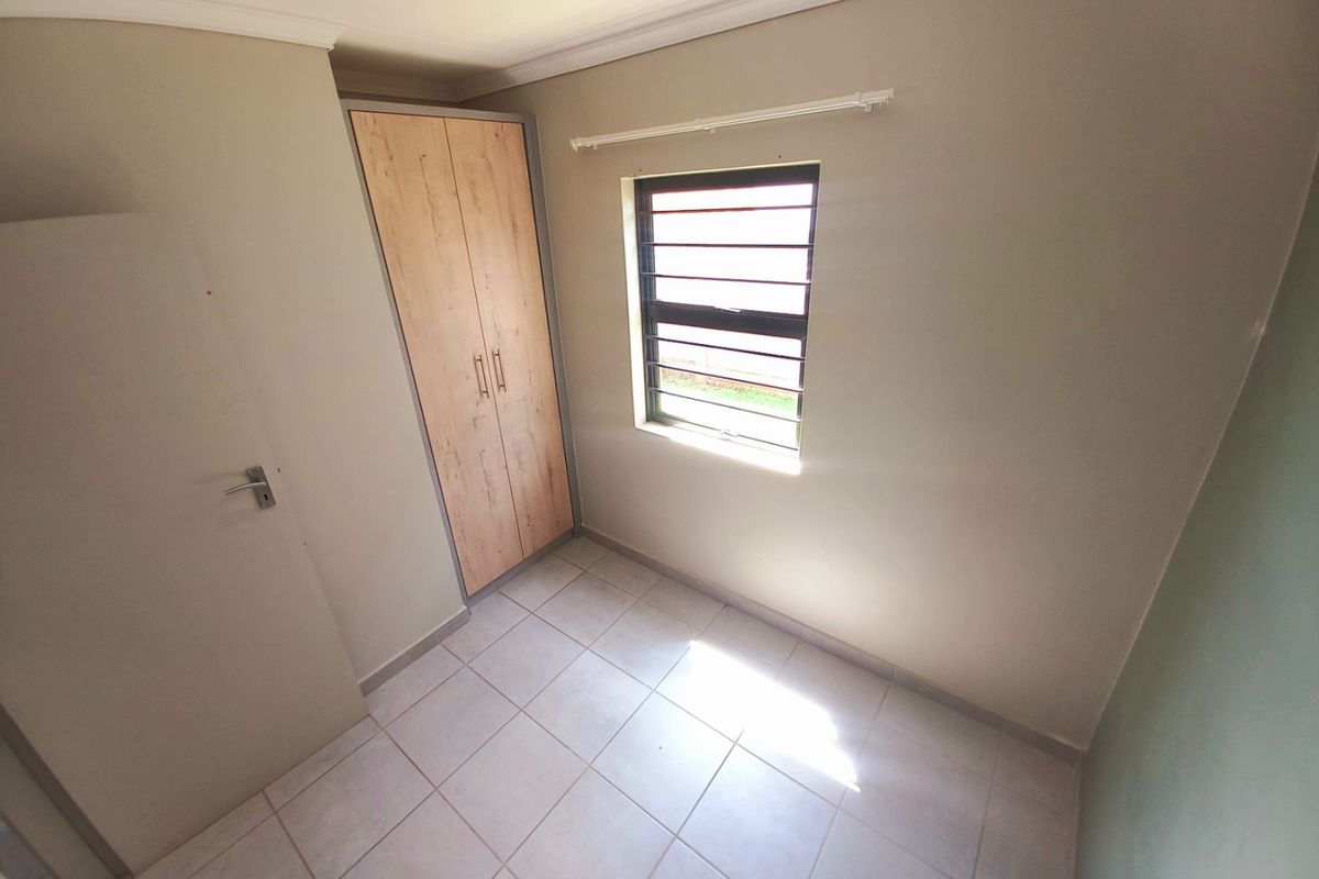 A compact bedroom featuring neutral tiled flooring, built-in wooden cabinetry, and a window with security bars.