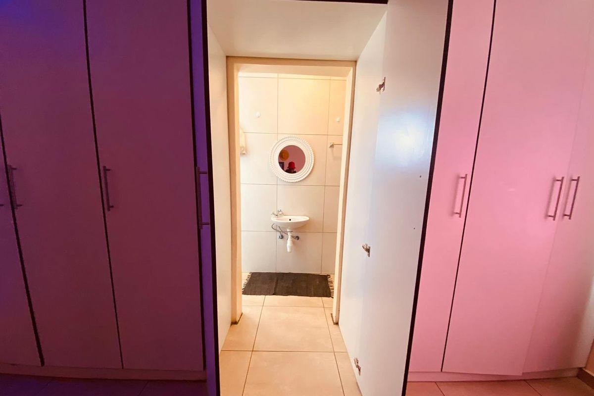 A view through a doorway into a bathroom featuring tiled walls, a wall-mounted basin, and built-in cupboards in the adjacent room.