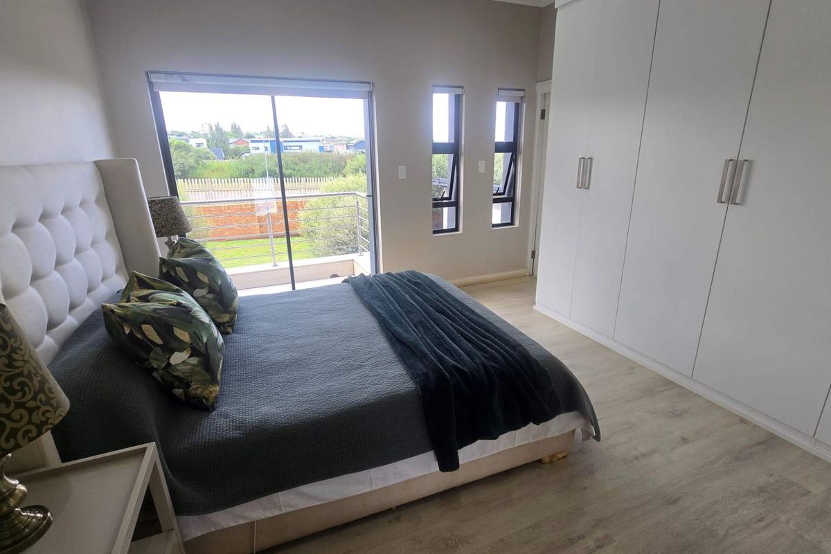 A well-maintained bedroom featuring built-in floor-to-ceiling wardrobes, light wood-look flooring, and sliding glass doors leading to a private balcony.