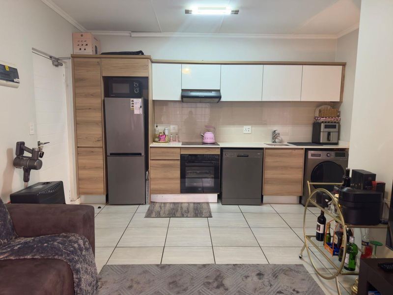 Modern open-plan kitchen featuring wood-grain and white cabinetry, integrated appliances, tiled flooring, and a functional layout suitable for contemporary apartment living.