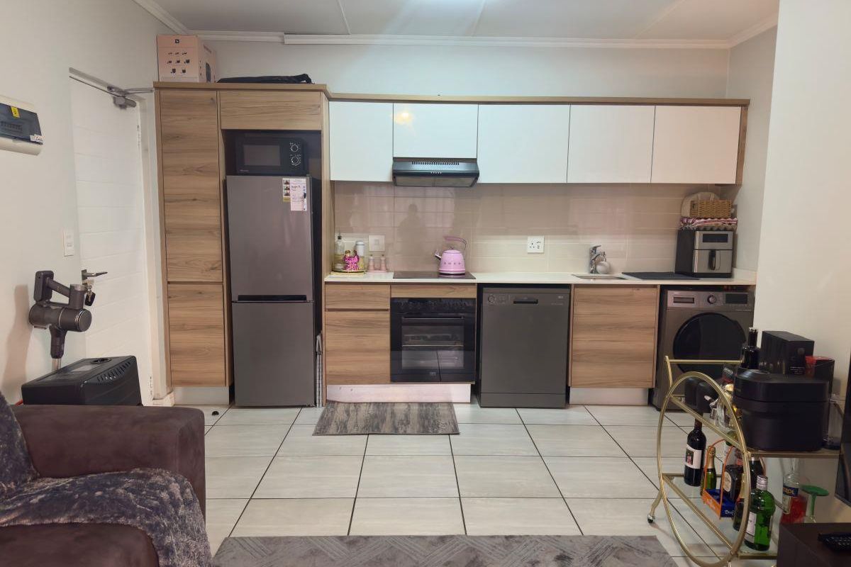 Modern open-plan kitchen featuring wood-grain and white cabinetry, integrated appliances, tiled flooring, and a functional layout suitable for contemporary apartment living.