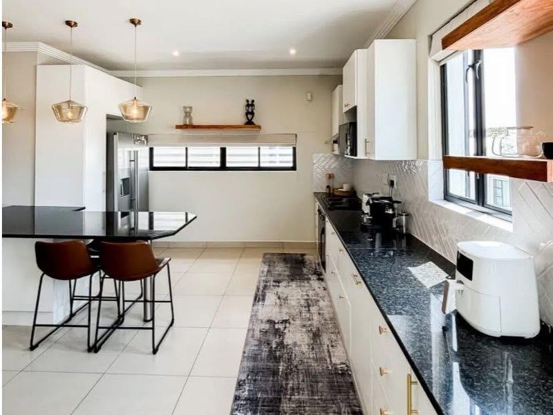 Modern kitchen featuring sleek white cabinetry, dark granite countertops, a breakfast bar, and stylish herringbone tile backsplash with ample natural light.