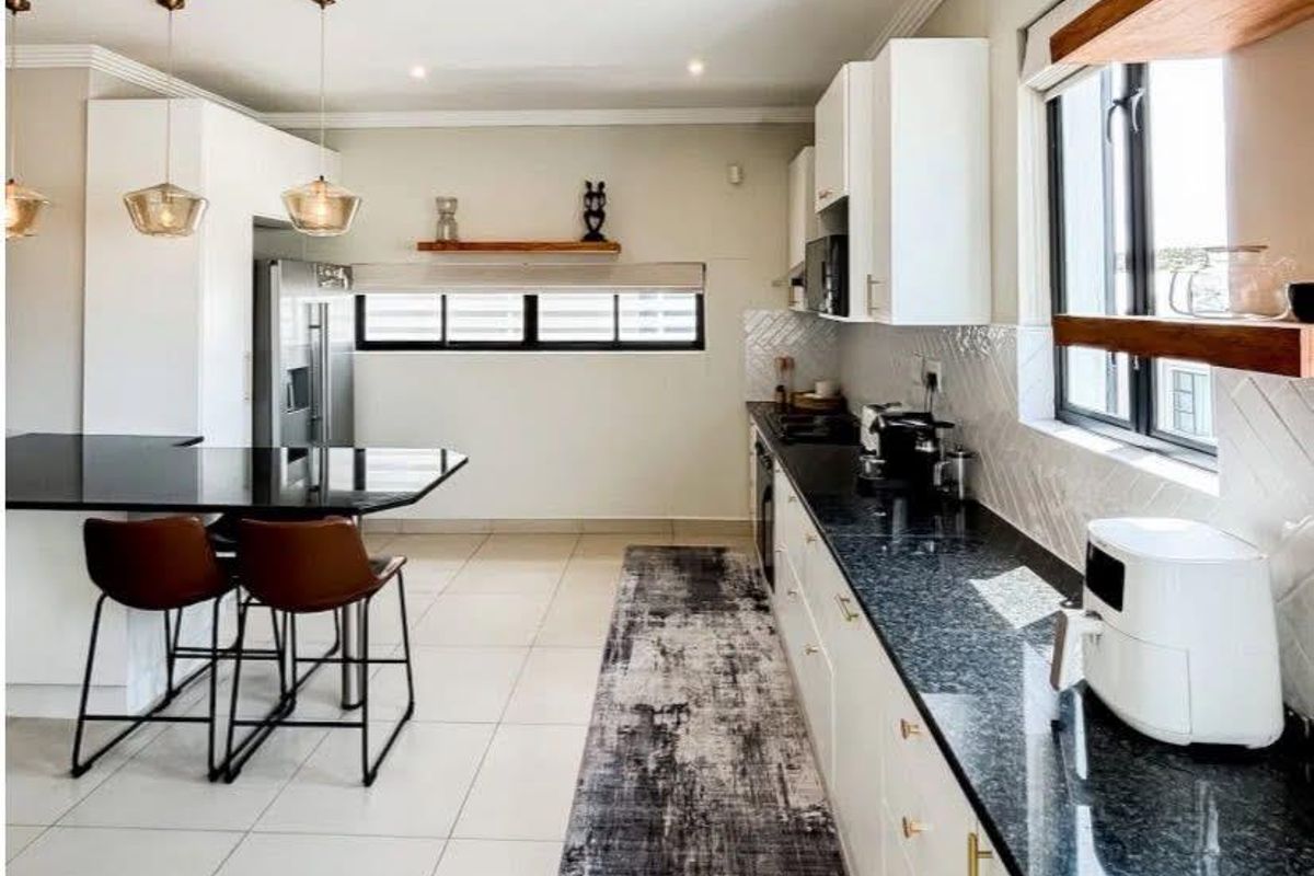 Modern kitchen featuring sleek white cabinetry, dark granite countertops, a breakfast bar, and stylish herringbone tile backsplash with ample natural light.