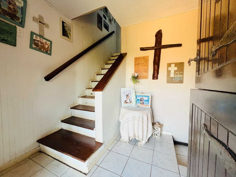 Entrance hall featuring a staircase with wooden handrail and tiled flooring, providing access to the upper level of the home.