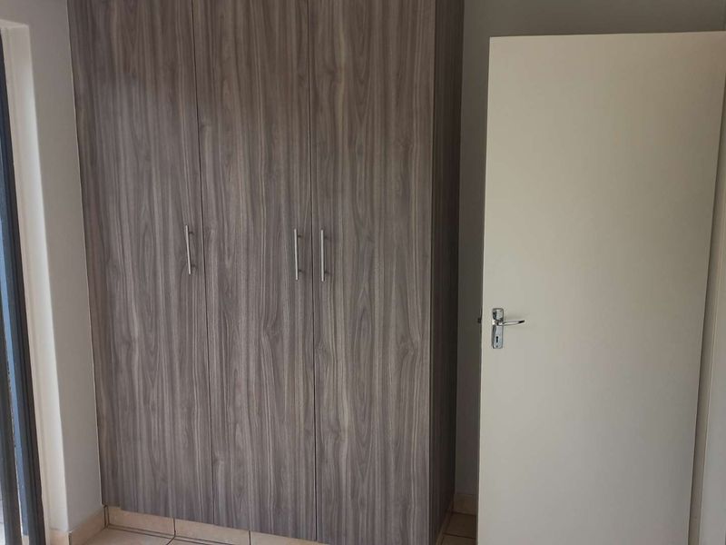 A clean, empty bedroom featuring modern wood-finish built-in cupboards, tiled flooring, and a sliding door providing access to an outdoor area.