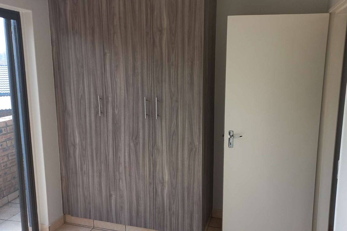 A clean, empty bedroom featuring modern wood-finish built-in cupboards, tiled flooring, and a sliding door providing access to an outdoor area.