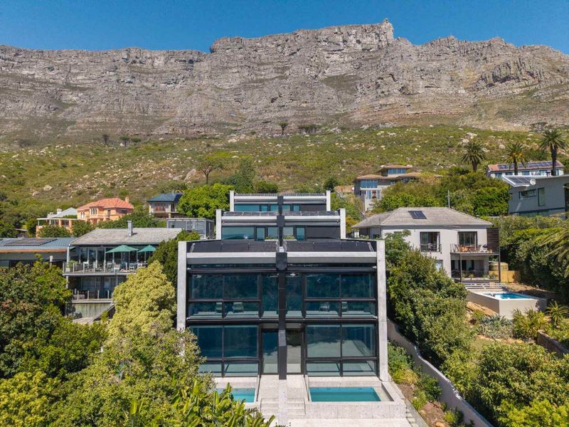 Aerial view of a modern multi-level residence featuring large glass facades, private swimming pools, and a dramatic mountain backdrop.