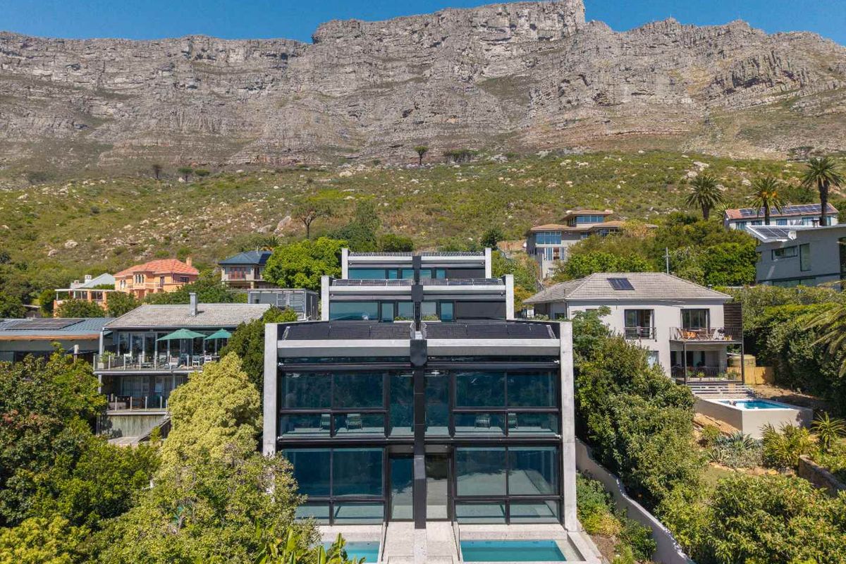 Aerial view of a modern multi-level residence featuring large glass facades, private swimming pools, and a dramatic mountain backdrop.