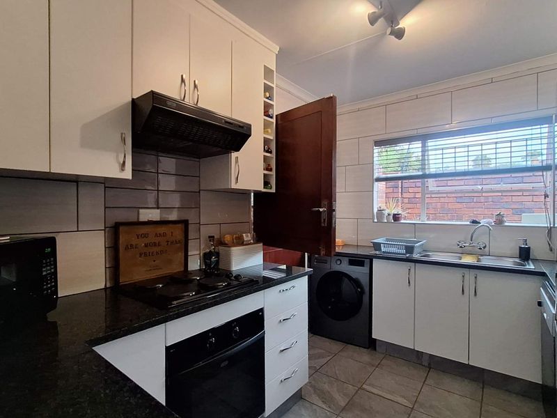 A functional kitchen featuring white cabinetry, granite countertops, a built-in oven with gas hob, extractor fan, and tiled finishes throughout.