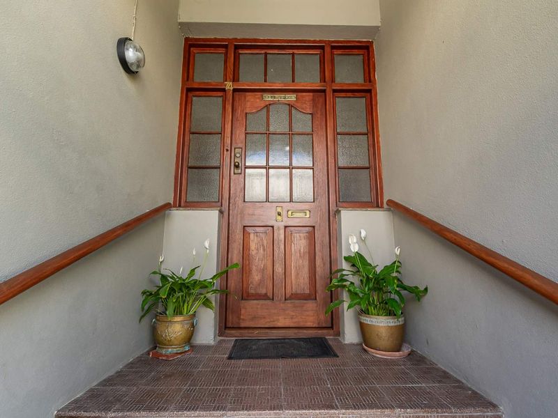 A classic timber front entrance featuring a paneled door with glass sidelights and transom, flanked by timber handrails on a tiled porch.