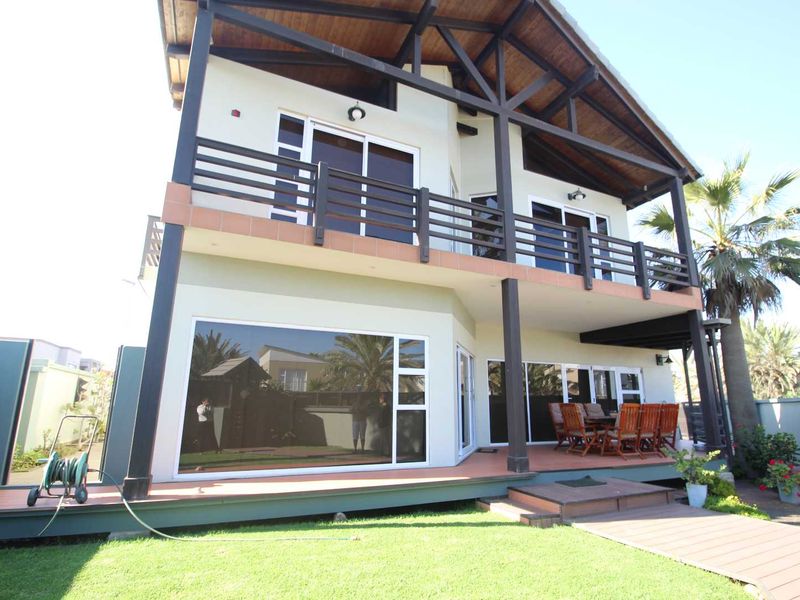 Rear view of a two-story house featuring a spacious ground-level deck, a covered upper balcony with timber trusses, and large sliding glass doors.