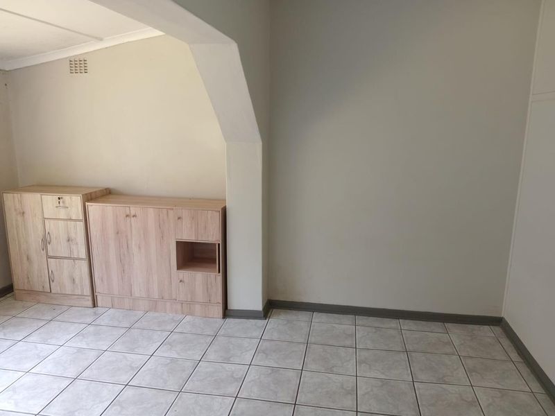 An empty living area featuring neutral tiled flooring, a structural archway, and simple wall finishes, providing a blank canvas for interior design.