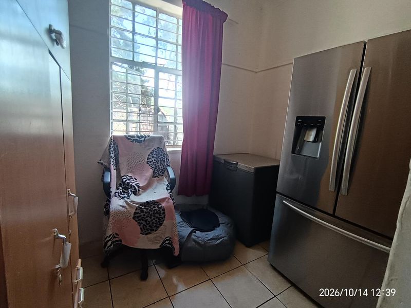 A functional scullery or utility area featuring tiled flooring, built-in cabinetry, and a window with security bars.