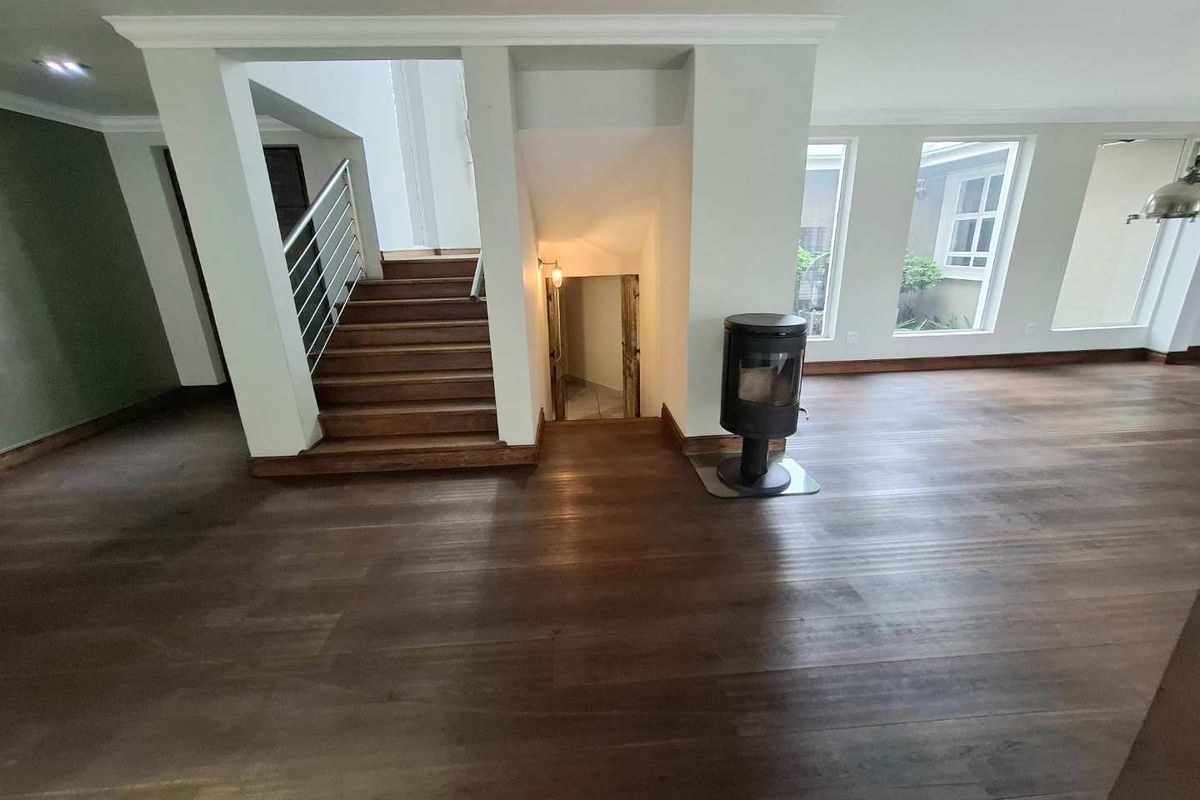 Spacious living area featuring dark hardwood flooring, a modern freestanding fireplace, and a central staircase with a metal balustrade.