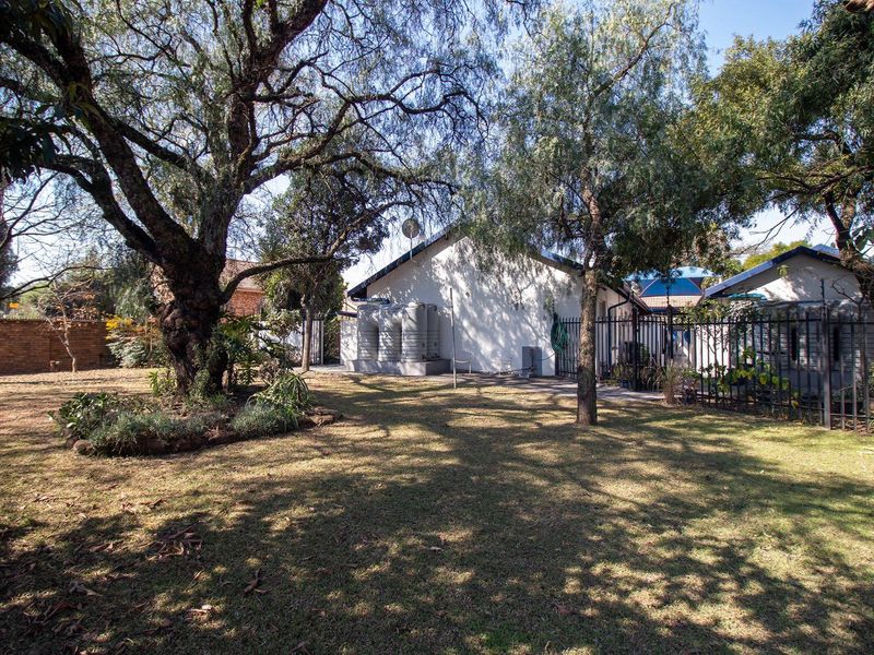 A spacious rear garden featuring mature trees, established lawn, metal perimeter fencing, and external water storage tanks.