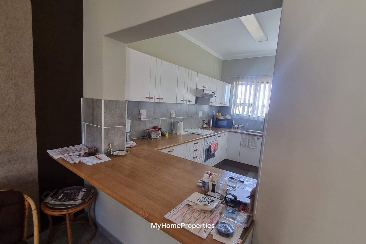 A functional kitchen featuring white cabinetry, a wooden breakfast bar, tiled backsplash, and built-in oven with extractor fan.