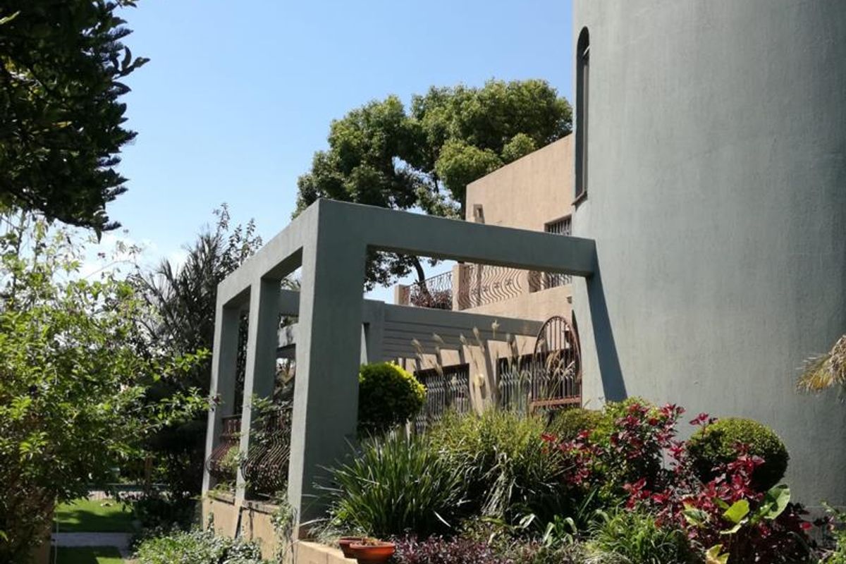 A view of the rear exterior of the property, featuring a distinctive cylindrical architectural element, a covered patio structure, and established garden landscaping.