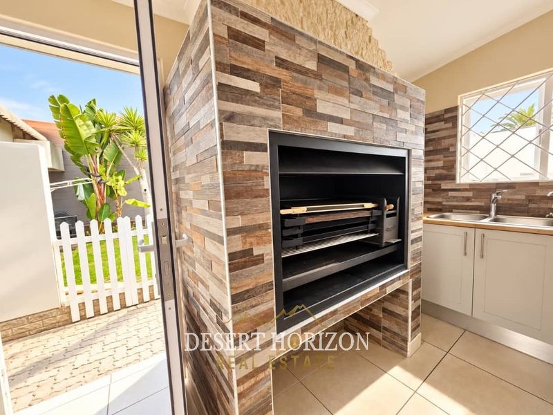 Covered patio area featuring a modern built-in braai with stone cladding, kitchenette cabinetry with a sink, and direct access to the garden.