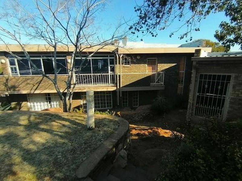 Rear view of a multi-level brick house featuring a balcony, security gates, and a landscaped garden with stone retaining walls and steps.