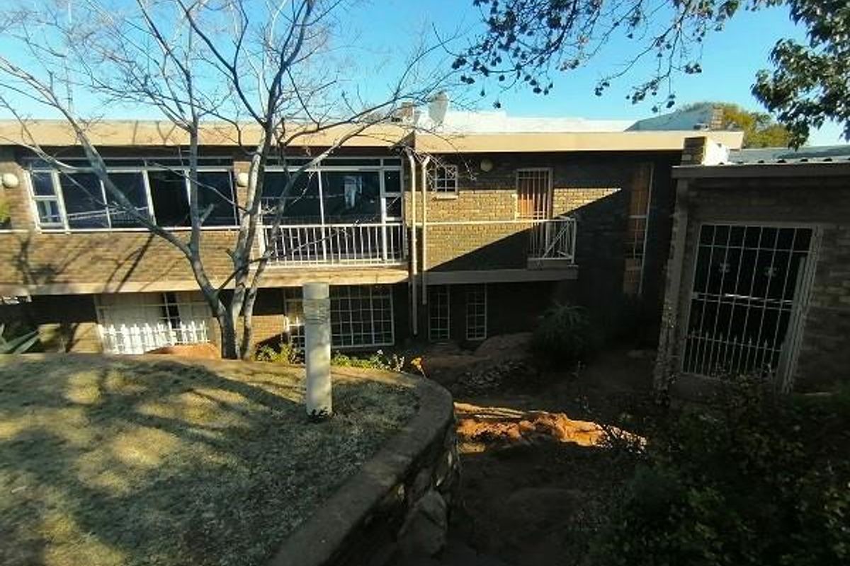 Rear view of a multi-level brick house featuring a balcony, security gates, and a landscaped garden with stone retaining walls and steps.