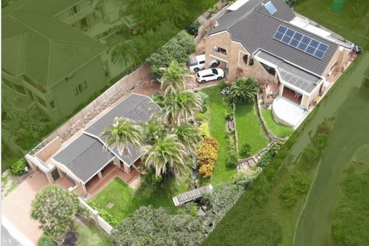 Aerial view of a residential property featuring a tiled roof, solar panels, landscaped garden, paved driveway, and a covered patio area.