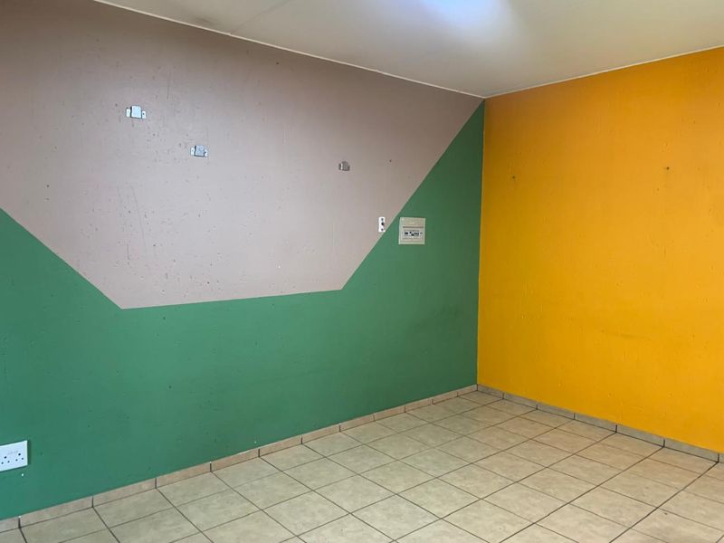 An empty living area featuring tiled flooring and multi-colored painted walls, equipped with a wall-mounted electrical distribution board and power outlets.