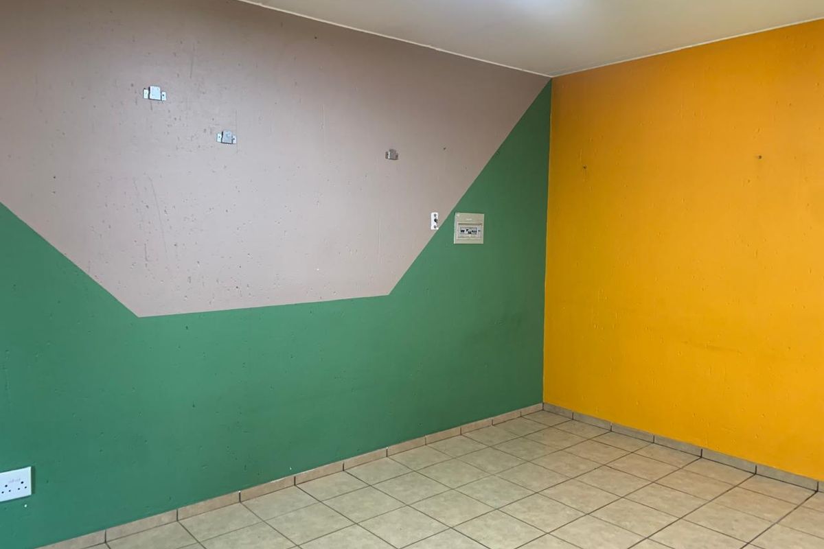 An empty living area featuring tiled flooring and multi-colored painted walls, equipped with a wall-mounted electrical distribution board and power outlets.