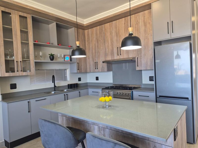 Modern kitchen featuring wood-grain and grey cabinetry, stone countertops, a central island, and integrated gas stove with extractor fan.