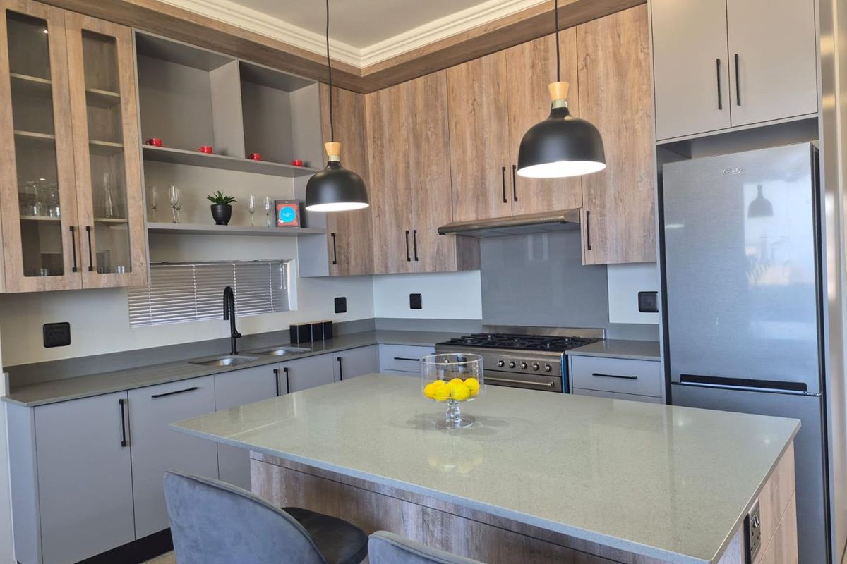 Modern kitchen featuring wood-grain and grey cabinetry, stone countertops, a central island, and integrated gas stove with extractor fan.